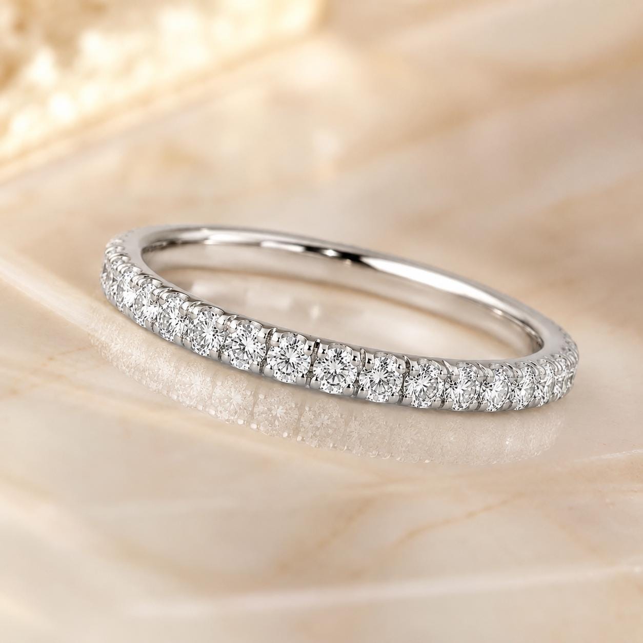 A diamond-encrusted ring with a row of small diamonds set in a silver band, resting on a marble surface.