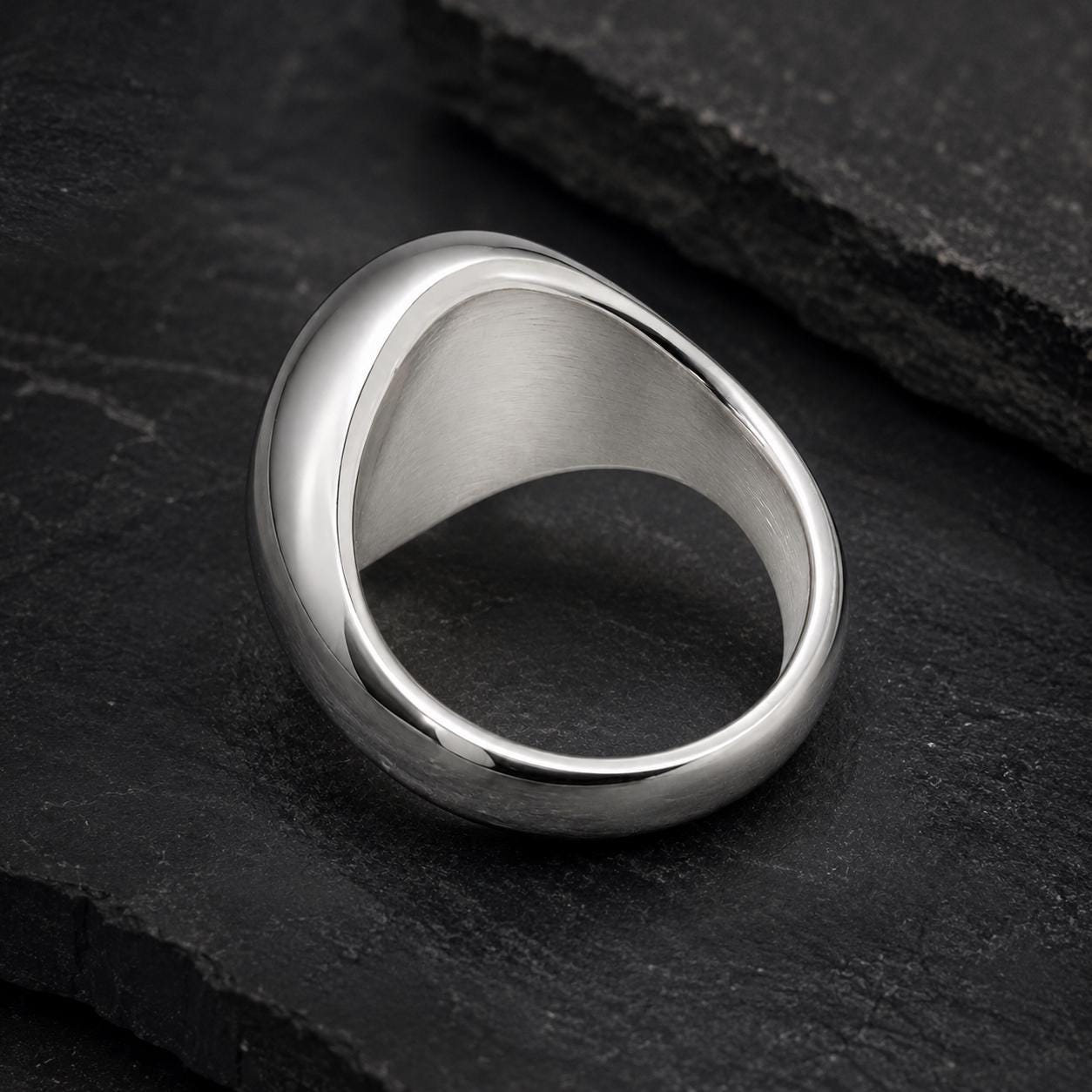 A silver ring with a unique, curved design rests on a dark surface.