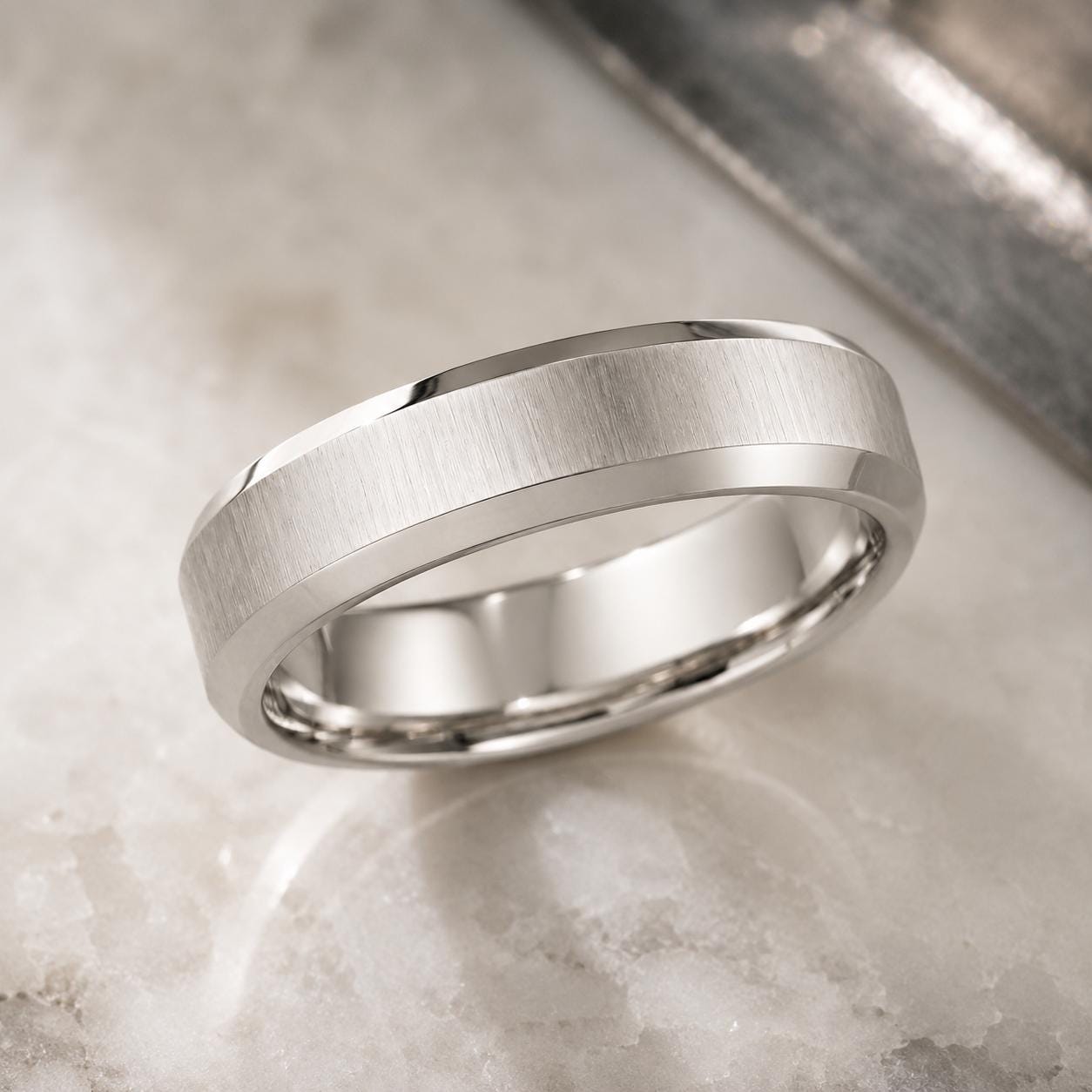 A silver-colored ring with a textured band is displayed on a marble surface.