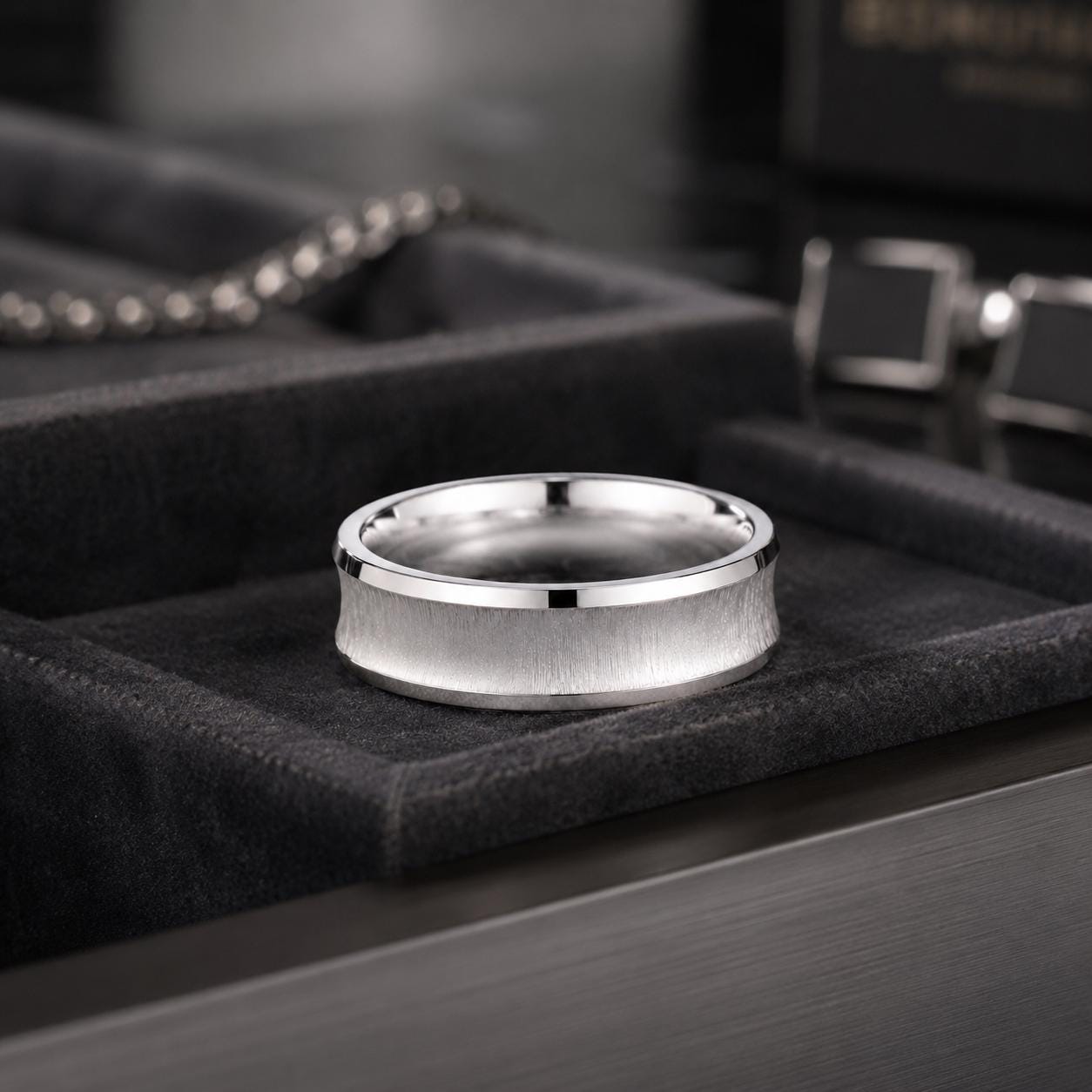 A silver ring with a textured band sits on a black velvet surface, surrounded by other jewelry items.