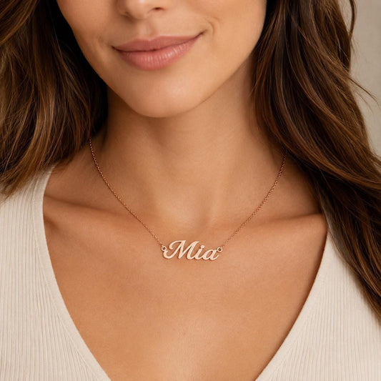A close-up of a woman's neck and chest area wearing a necklace with the name "Mia" engraved on it.