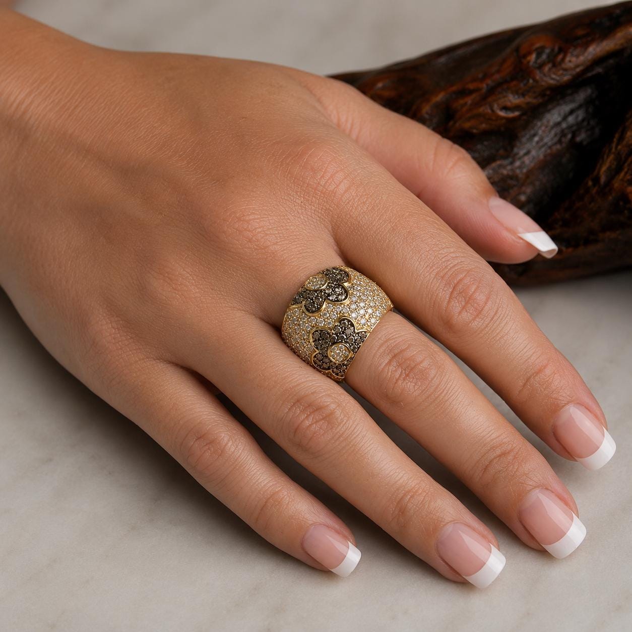 A close-up of a person's hand wearing a gold ring with a floral design.