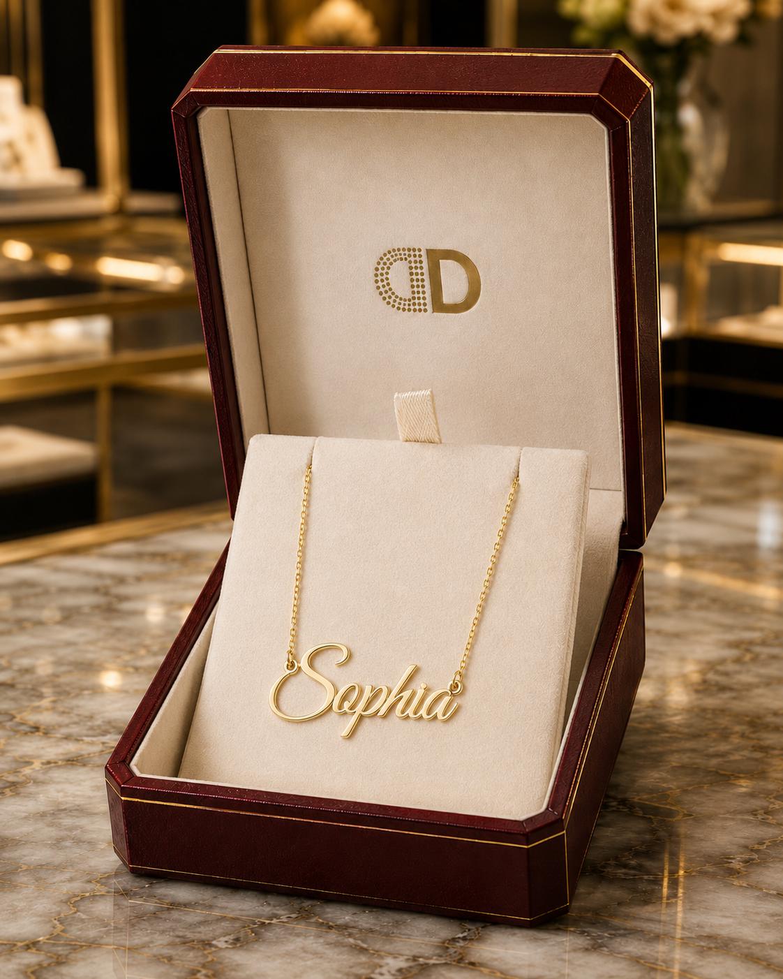 A gold necklace with the name "Sophia" engraved on it, displayed in a burgundy jewelry box.
