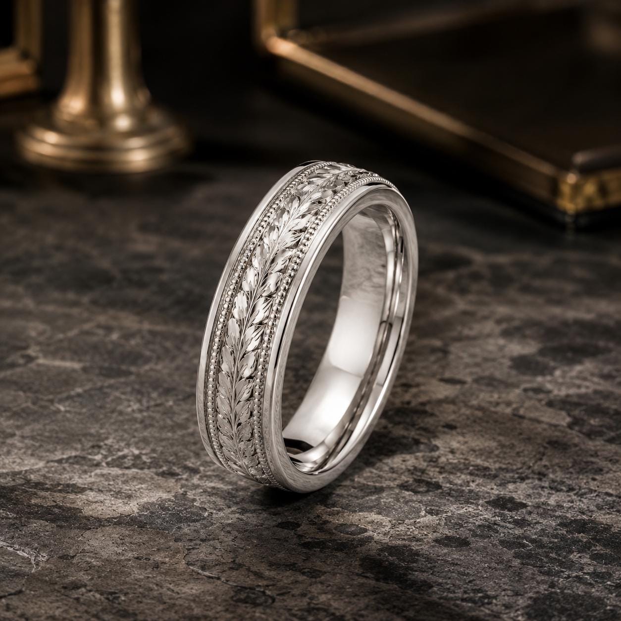 A silver ring with a decorative band featuring leaf-like patterns is displayed on a dark surface.