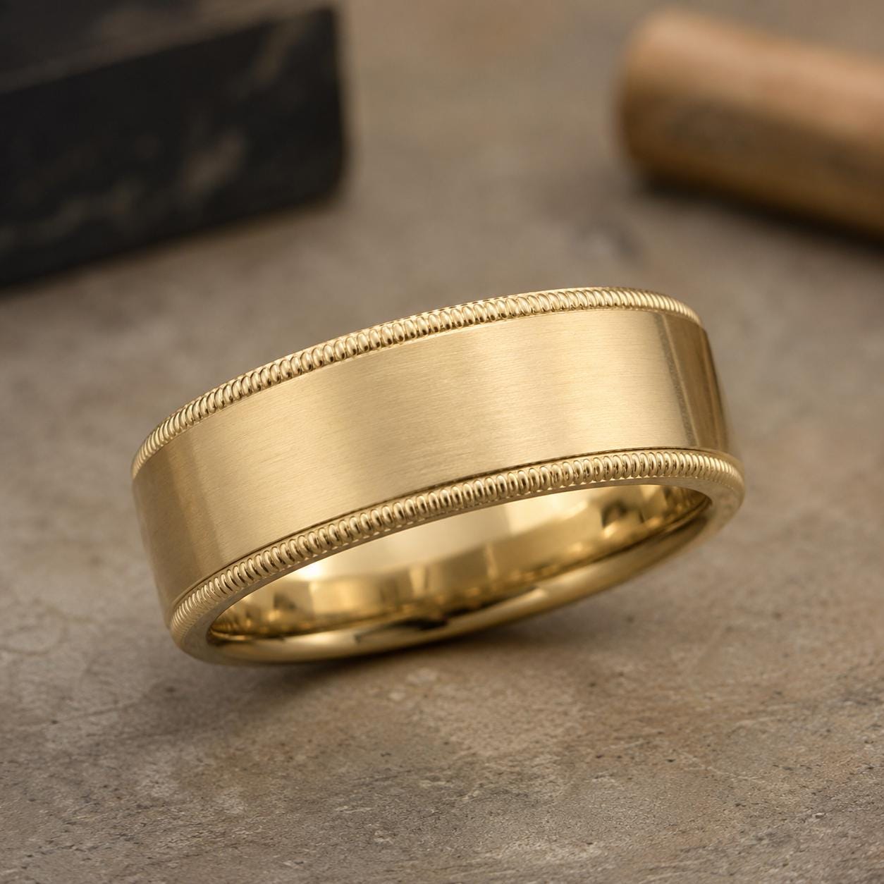 A gold-colored ring with a smooth, shiny surface sits on a textured surface.
