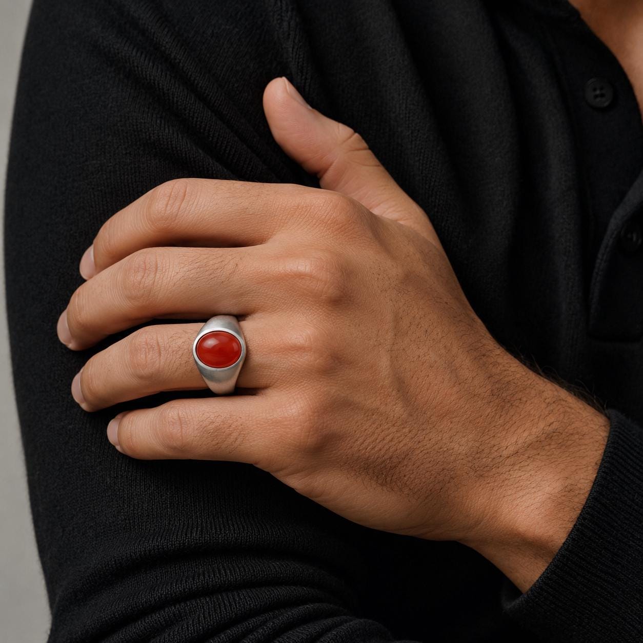 A close-up of a person's hand wearing a silver ring with a red gemstone.