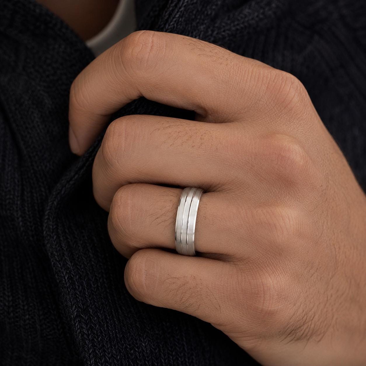 A close-up of a person's hand wearing a silver ring on the ring finger.