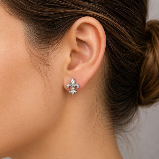A close-up of a woman's ear wearing a diamond earring with a fleur-de-lis design.
