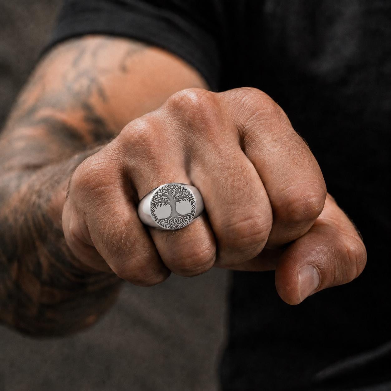 A close-up of a person's hand wearing a silver ring with a tree design.