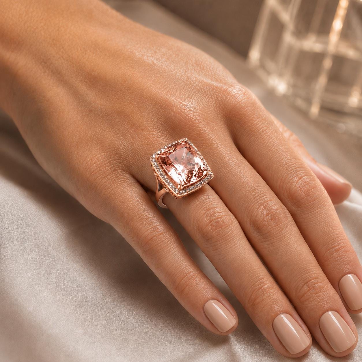 A close-up of a hand wearing a large, pink gemstone ring with a halo of smaller diamonds around it.