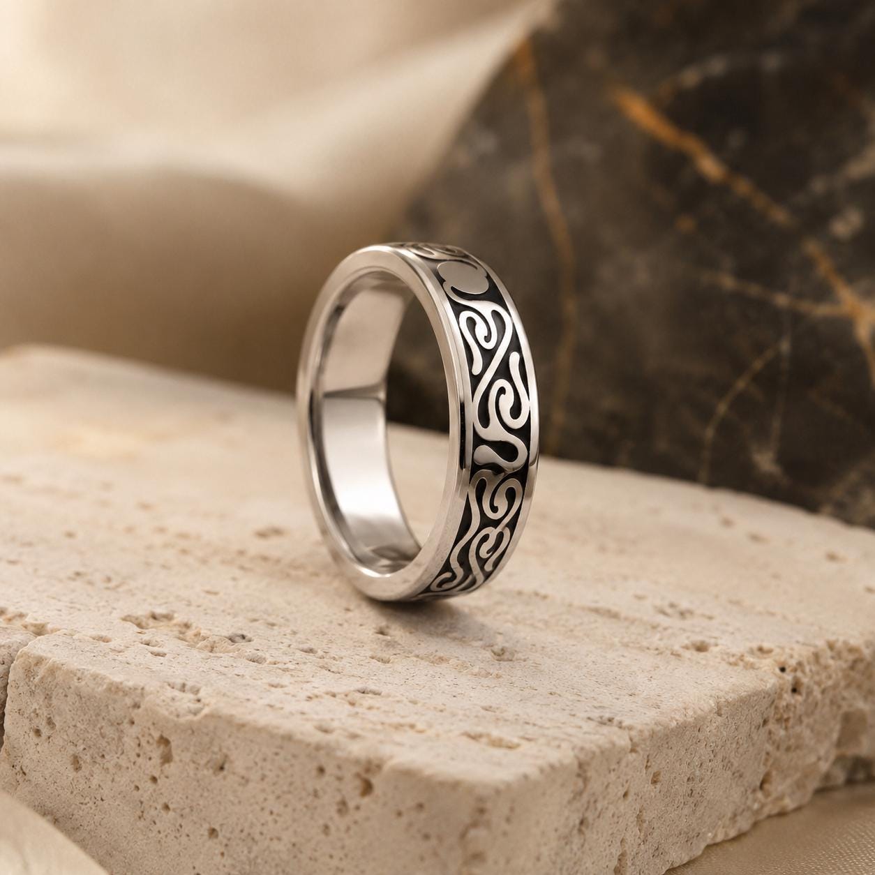 A silver ring with a black and white spiral design sits on a stone surface.