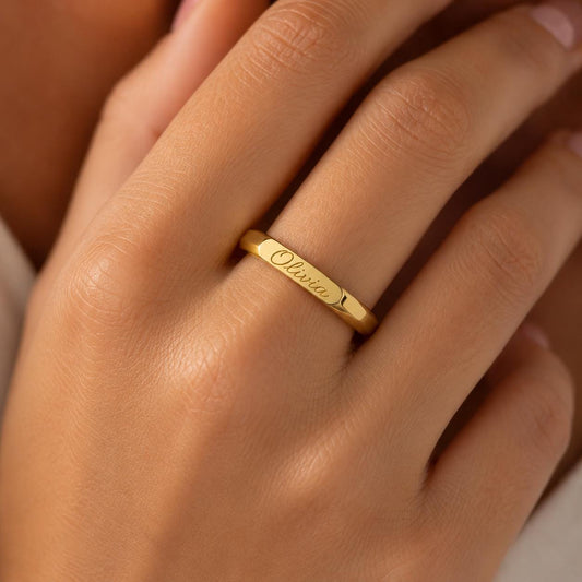A close-up of a person's hand wearing a gold ring with the name "Olivia" engraved on it.