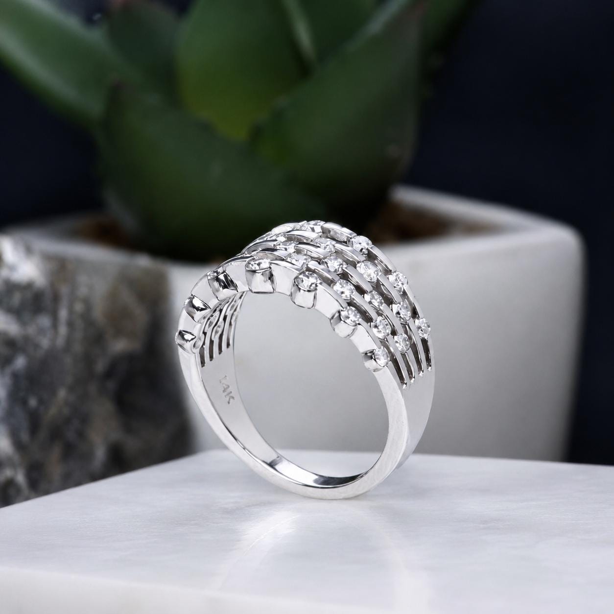 A silver ring with a unique design, featuring a curved band and a row of small diamonds or stones set in it, is displayed on a white surface.
