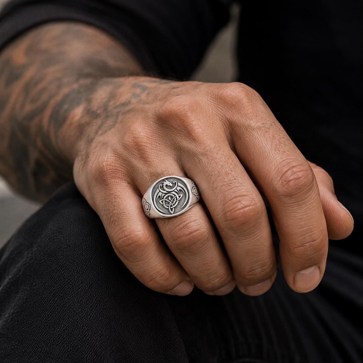 A close-up of a person's hand wearing a silver ring with a dragon design.