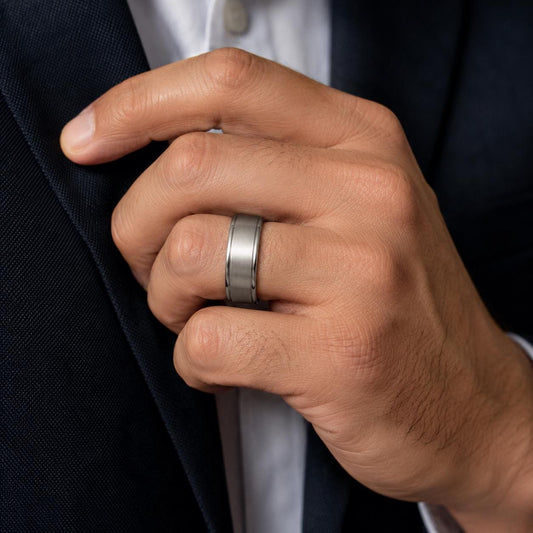A close-up of a person's hand wearing a silver ring, with a suit jacket visible in the background.