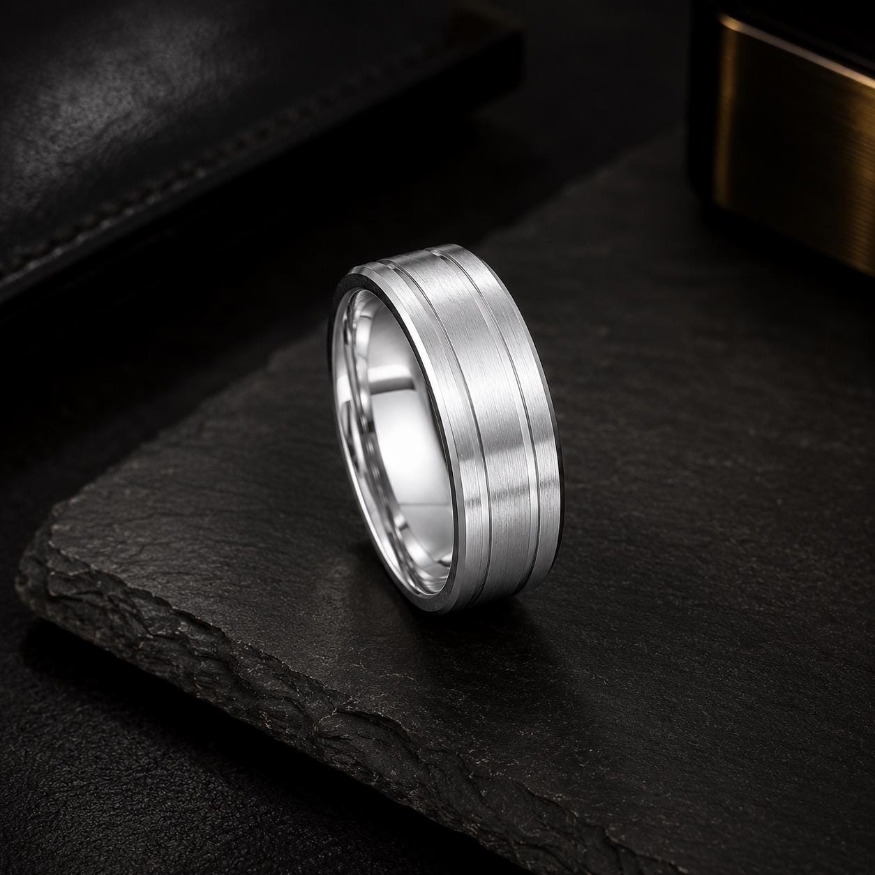A silver ring with a unique design sits on a dark surface, surrounded by other objects.