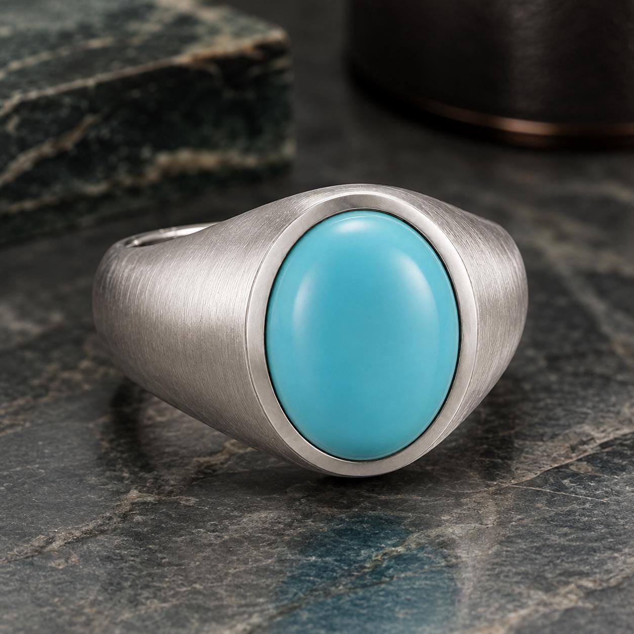A silver ring with a turquoise stone set in the center, resting on a dark surface.
