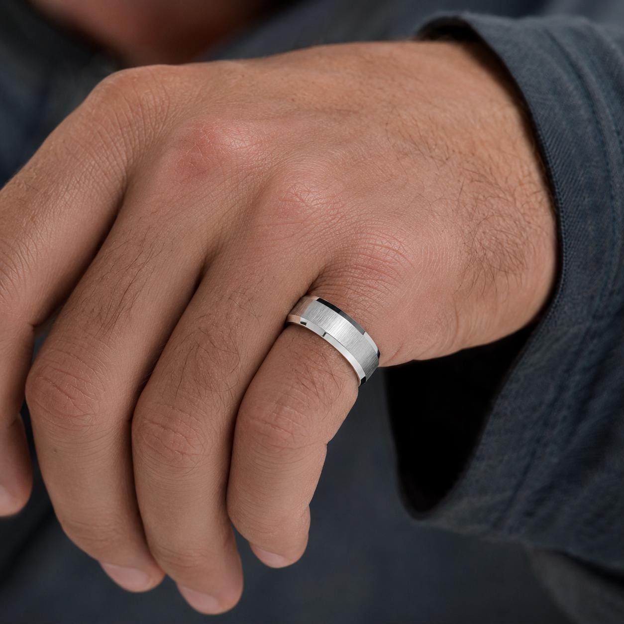 A close-up of a person's hand wearing a silver ring on the ring finger.