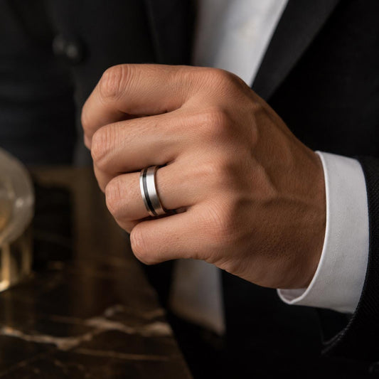 A close-up of a person's hand wearing a silver ring on the ring finger.