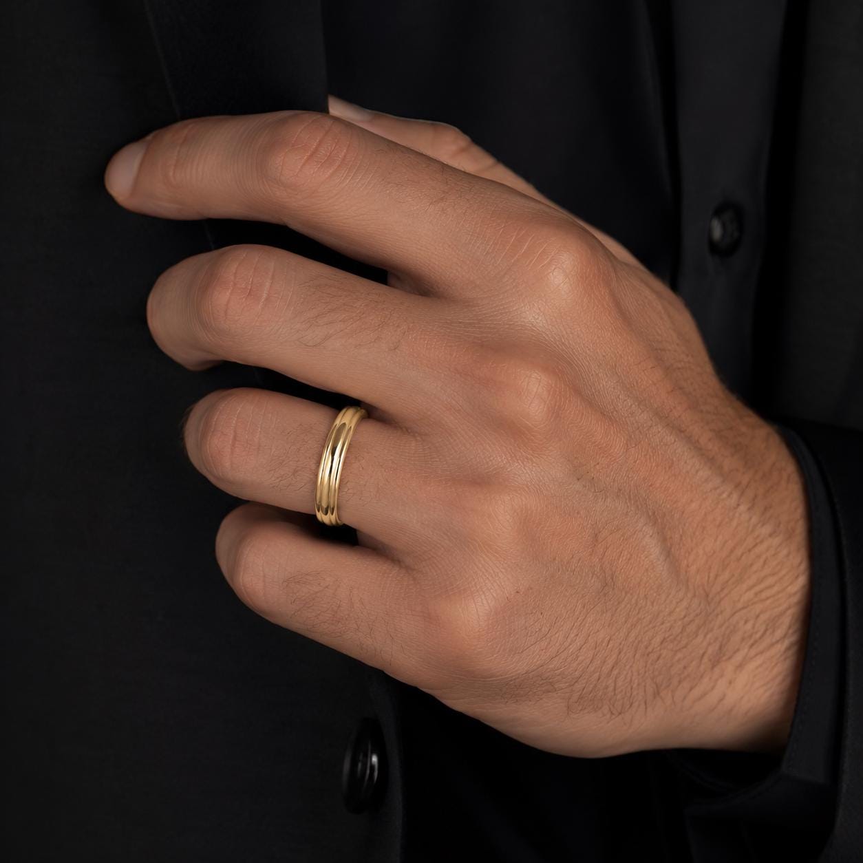 A close-up of a person's hand wearing a gold ring, with a black jacket visible in the background.