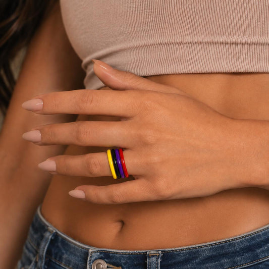 A close-up of a person's hand wearing a ring with colorful bands, wearing a beige top and blue jeans.