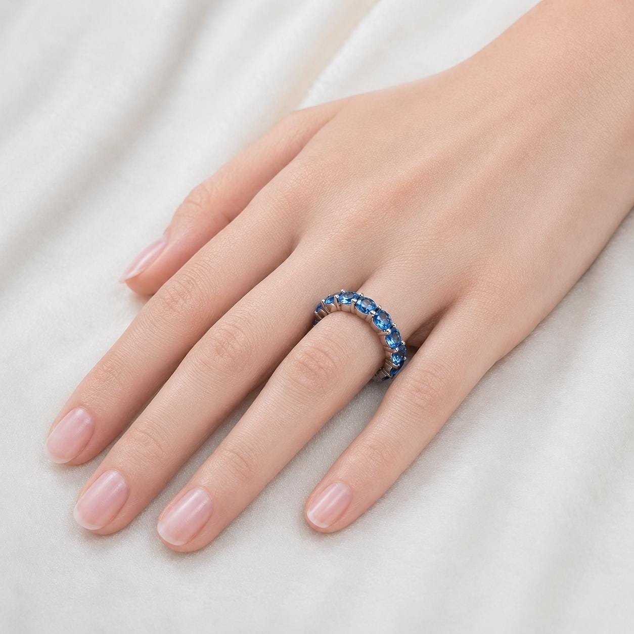 A close-up of a hand wearing a ring with blue gemstones.