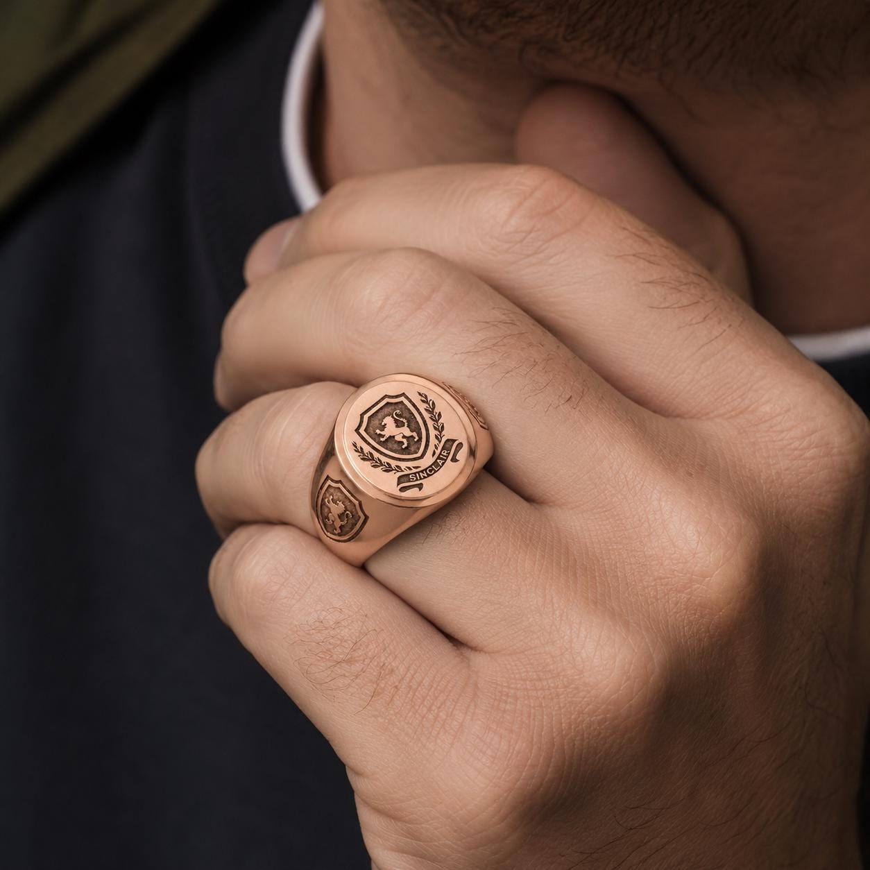 A close-up of a person's hand wearing a gold-colored ring with a shield-shaped emblem on it.