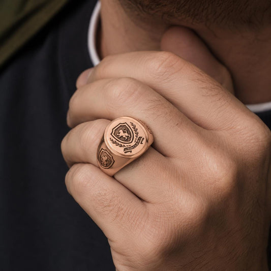 A close-up of a person's hand wearing a gold-colored ring with a shield-shaped emblem on it.