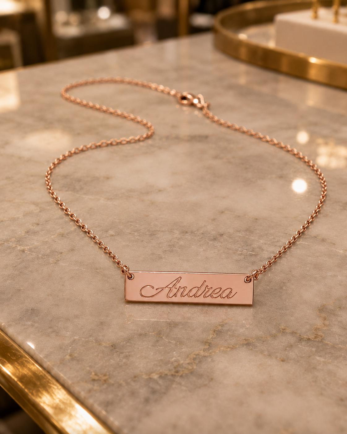 A necklace with a personalized nameplate is displayed on a marble countertop.