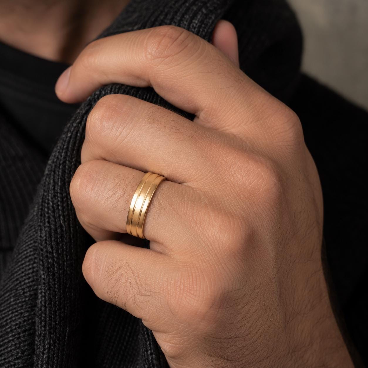 A close-up of a person's hand wearing a gold ring, with a dark sweater partially visible behind the hand.