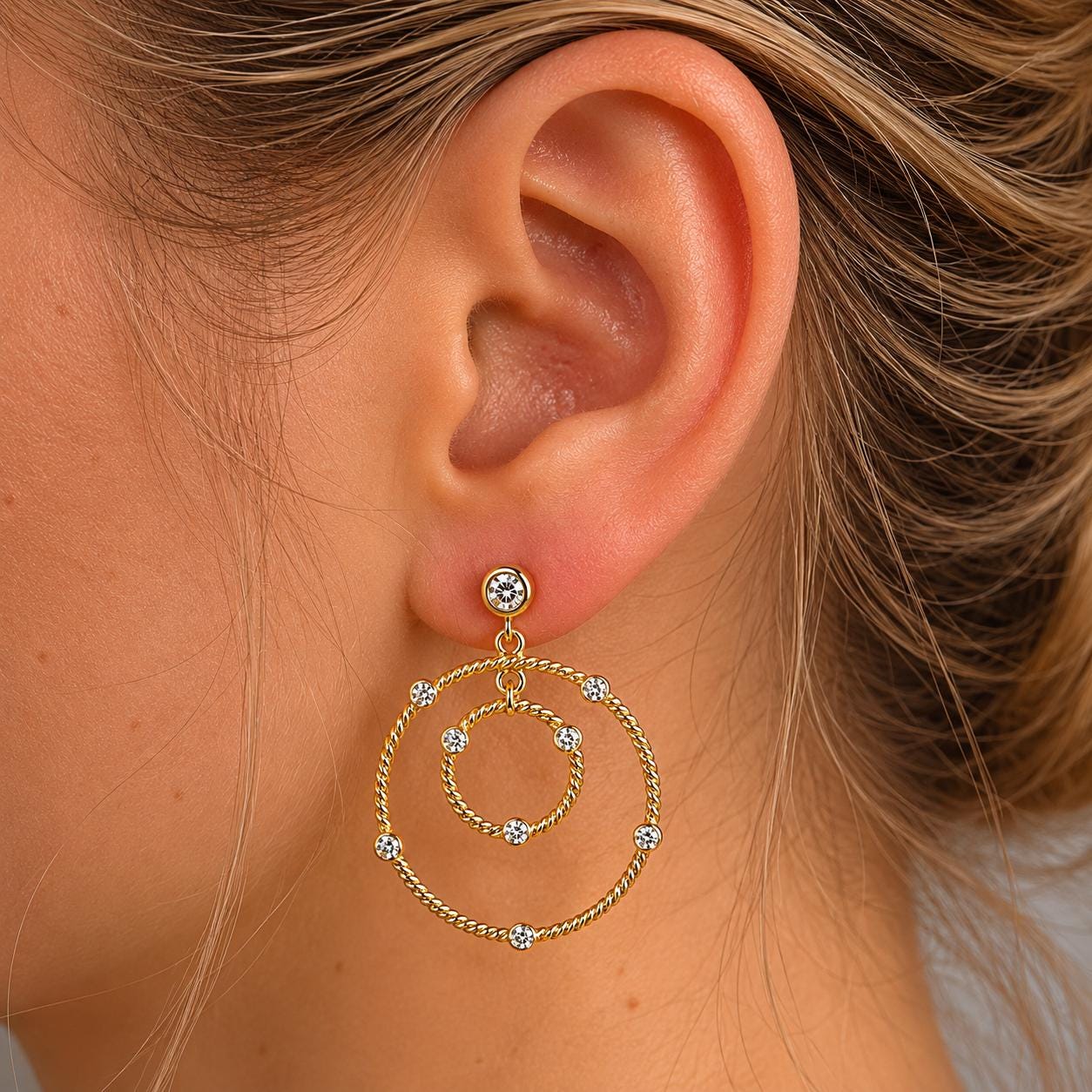 A close-up view of a woman's ear adorned with a pair of gold hoop earrings featuring a circular design with small diamonds.