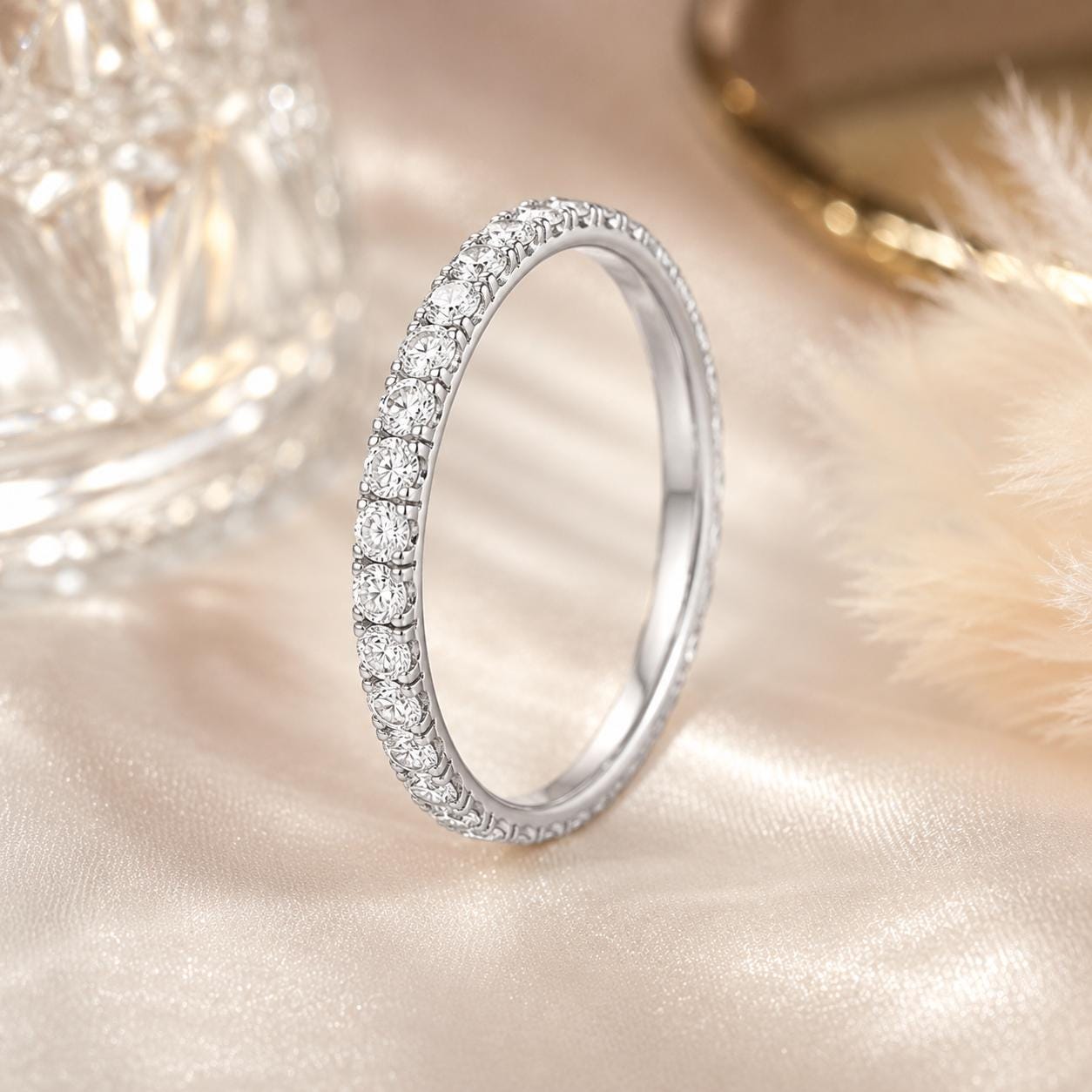 A silver ring with a row of small diamonds set in the band is displayed on a light pink fabric background.