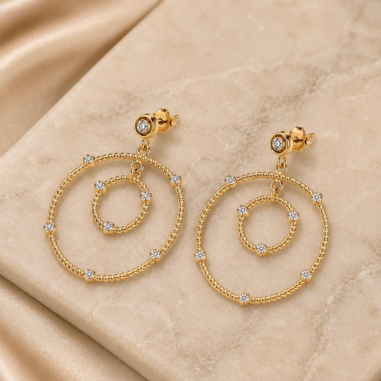 A pair of gold earrings with diamond-encrusted circular designs, placed on a beige surface.