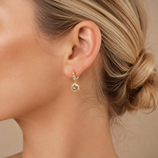 A close-up view of a woman's ear adorned with a gold earring featuring a hexagon-shaped charm.