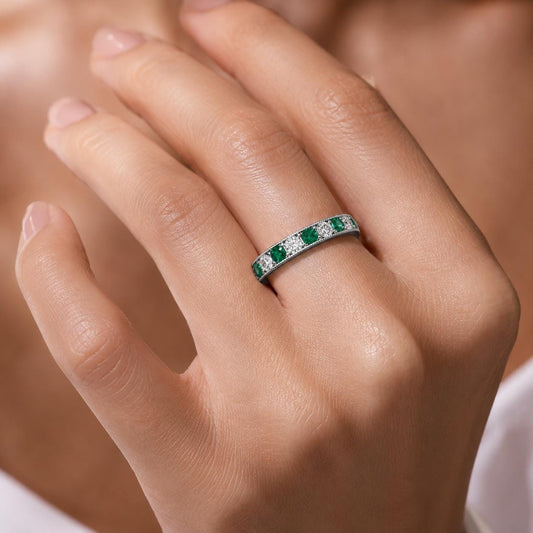 A close-up of a person's hand wearing a ring with a row of green gemstones.