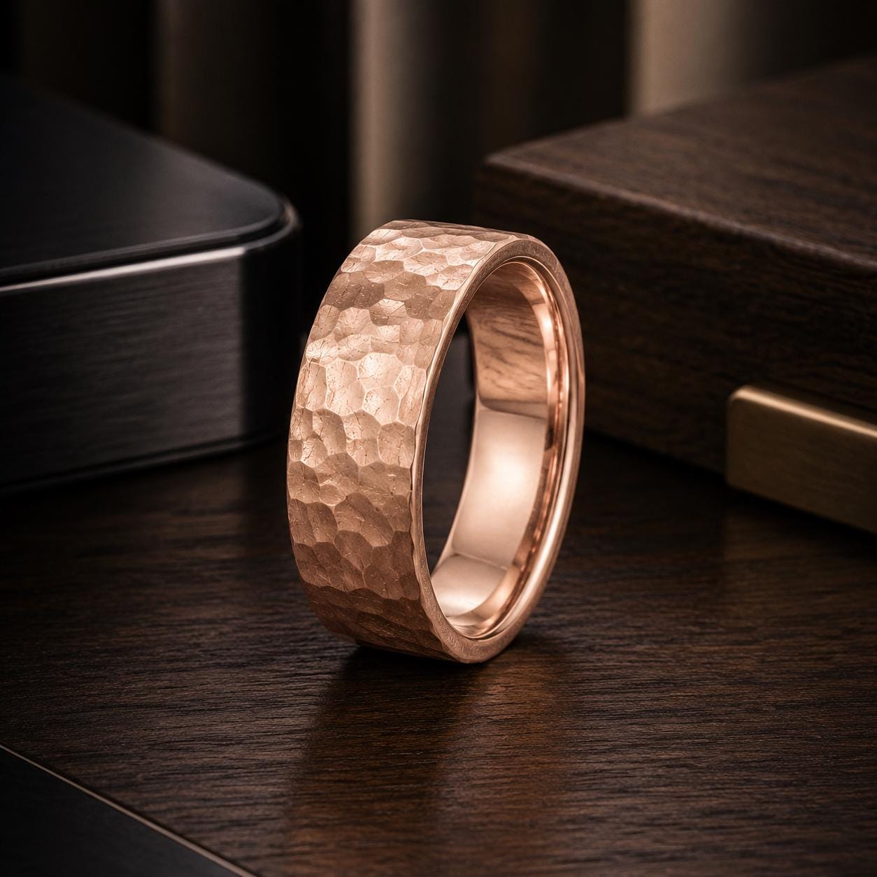 A shiny, textured copper-colored ring is displayed on a dark wooden surface, with a black object in the background.