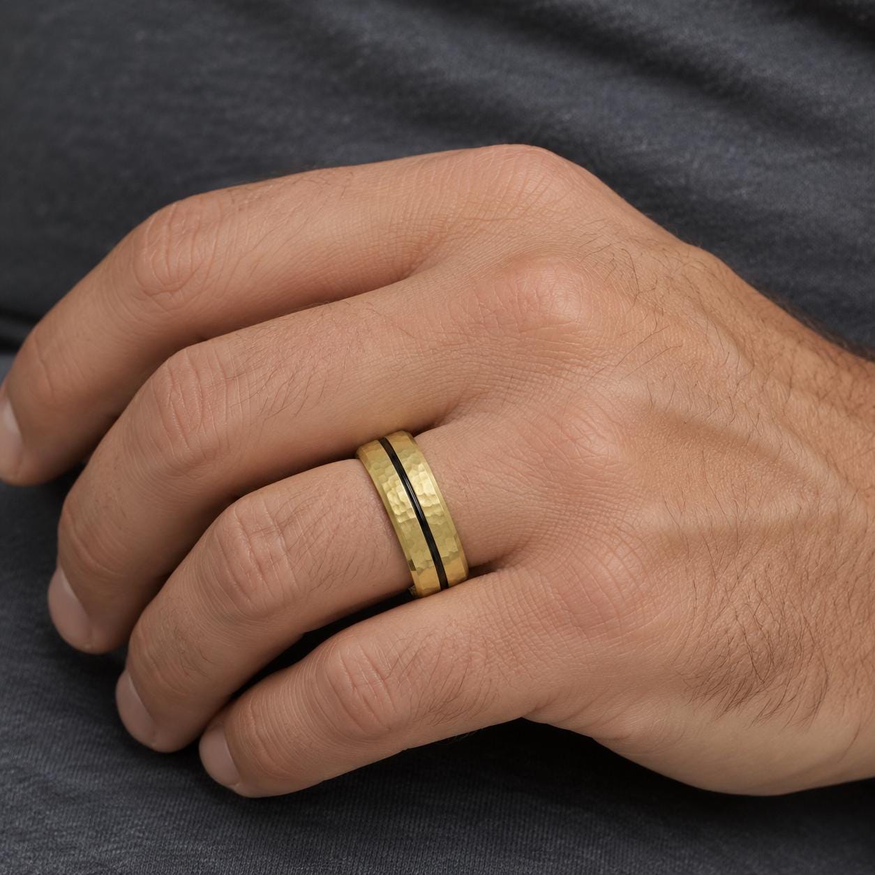 A close-up of a person's hand wearing a gold ring with a black band.
