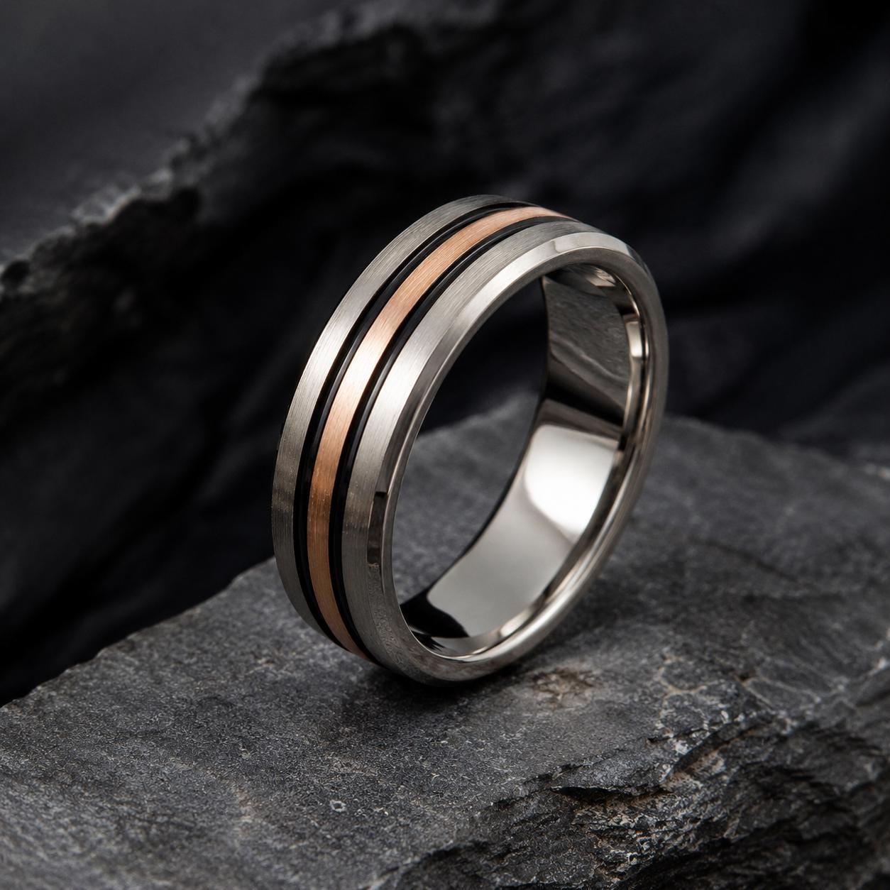 A silver ring with a thin band of copper and silver sits on a dark gray rock.