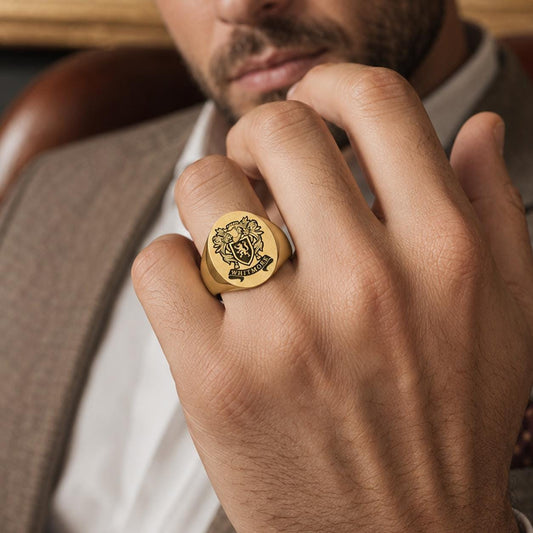 A close-up of a person's hand wearing a gold ring with a crest design.