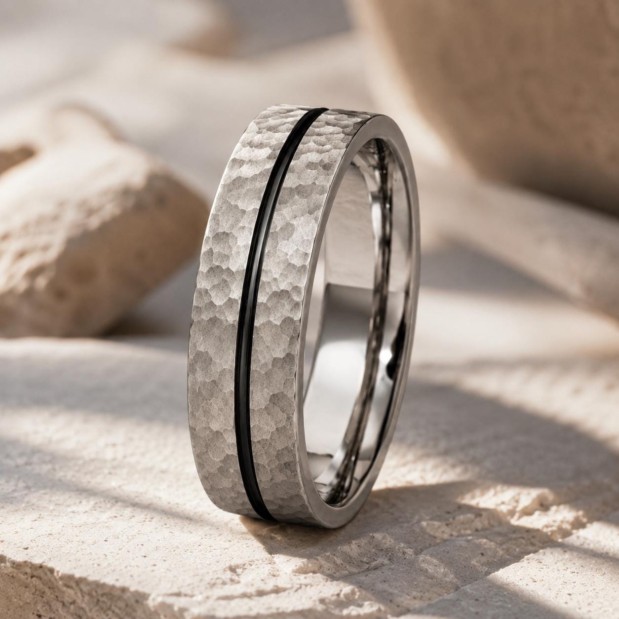 A silver ring with a textured band and a black line running through it, resting on a beige surface.