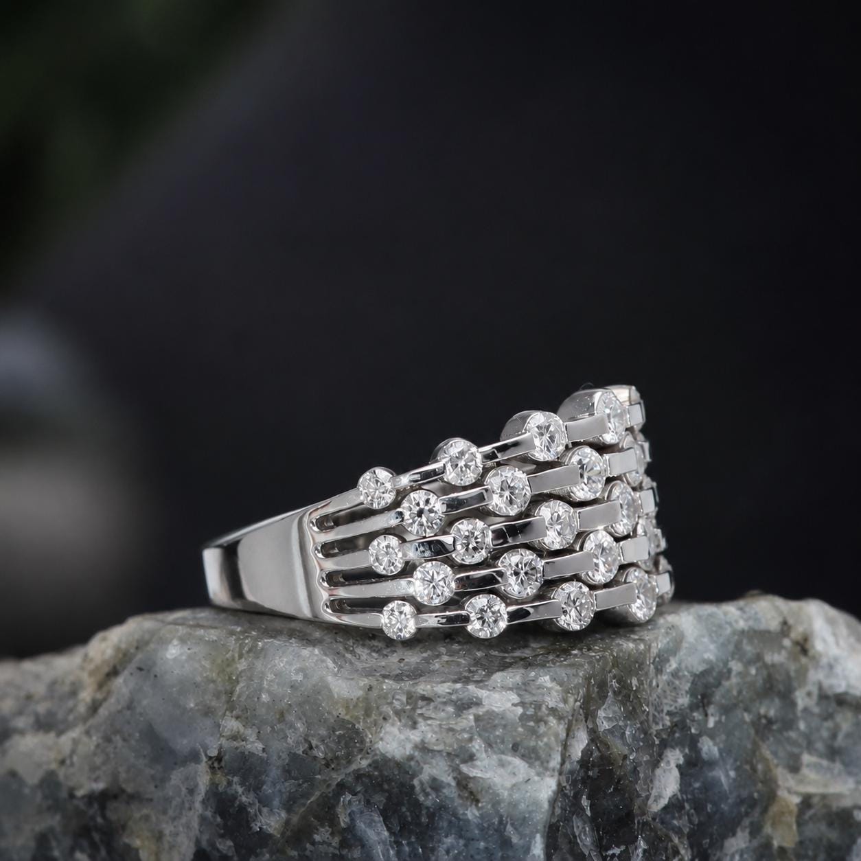 A silver ring with a row of diamonds set in a band, resting on a rock.
