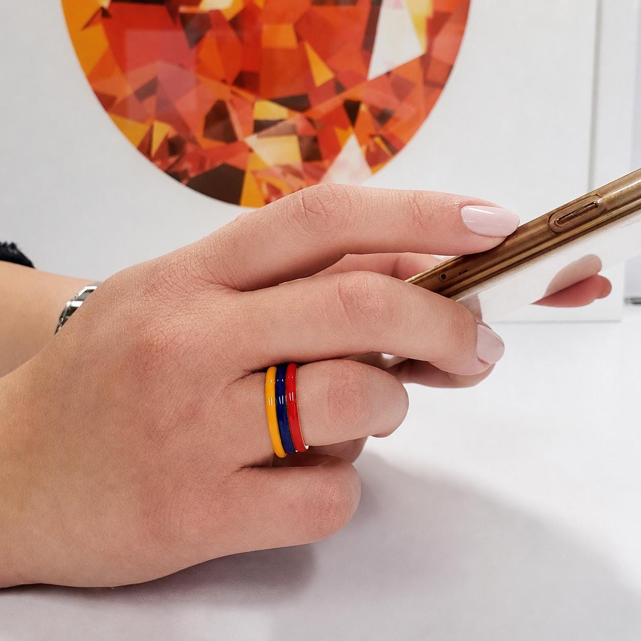 A person's hand holding a smartphone, with a colorful ring on the finger.