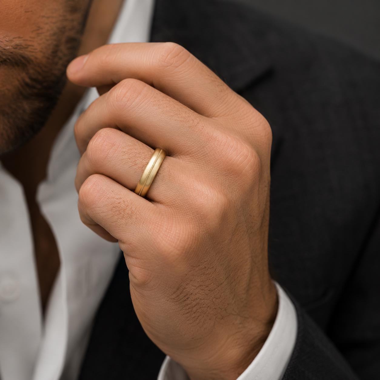 A close-up of a man's hand wearing a gold wedding ring, with a suit jacket visible in the background.