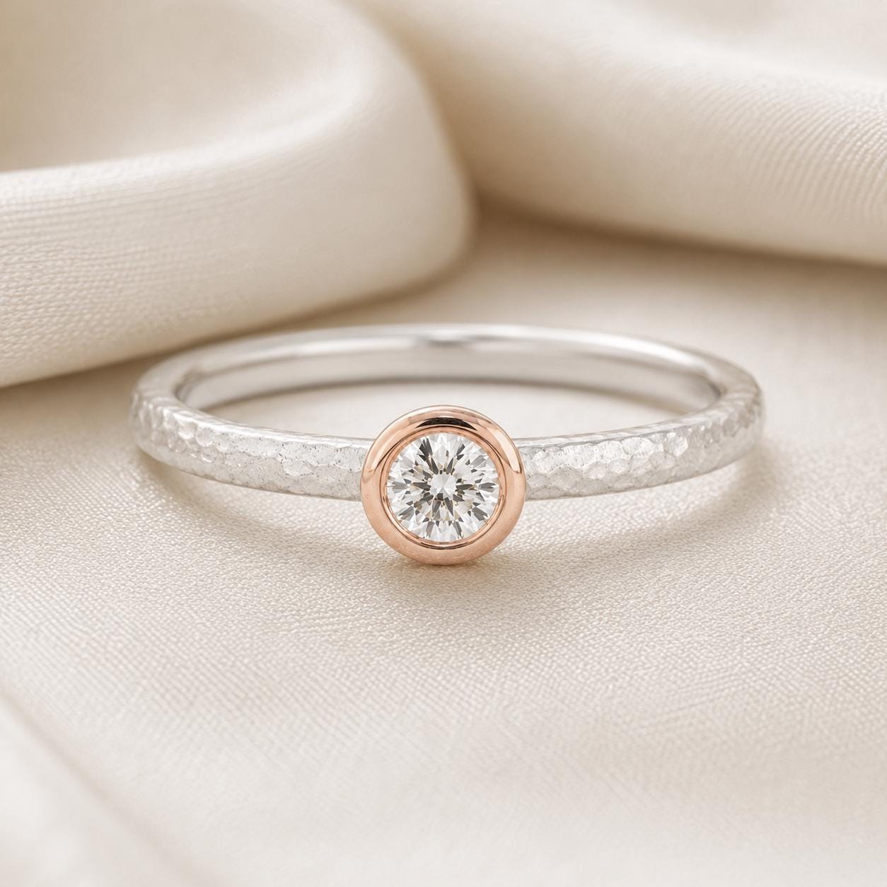 A simple yet elegant ring with a large diamond set in the center, resting on a white fabric background.