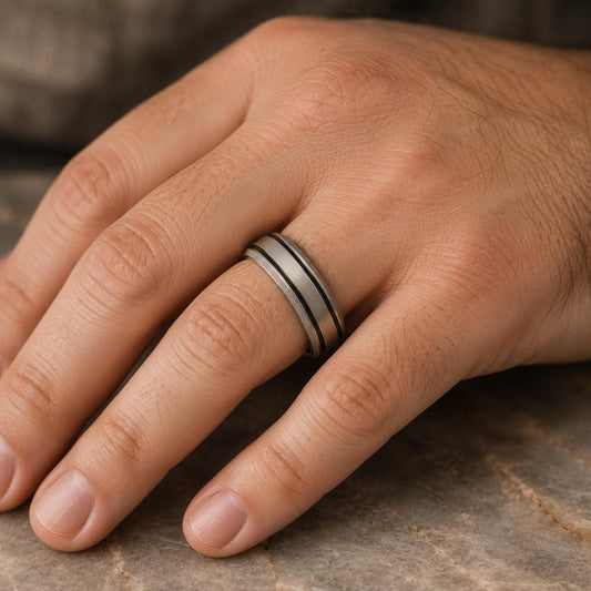 A close-up image of a hand wearing a silver ring with a black stripe on the band.